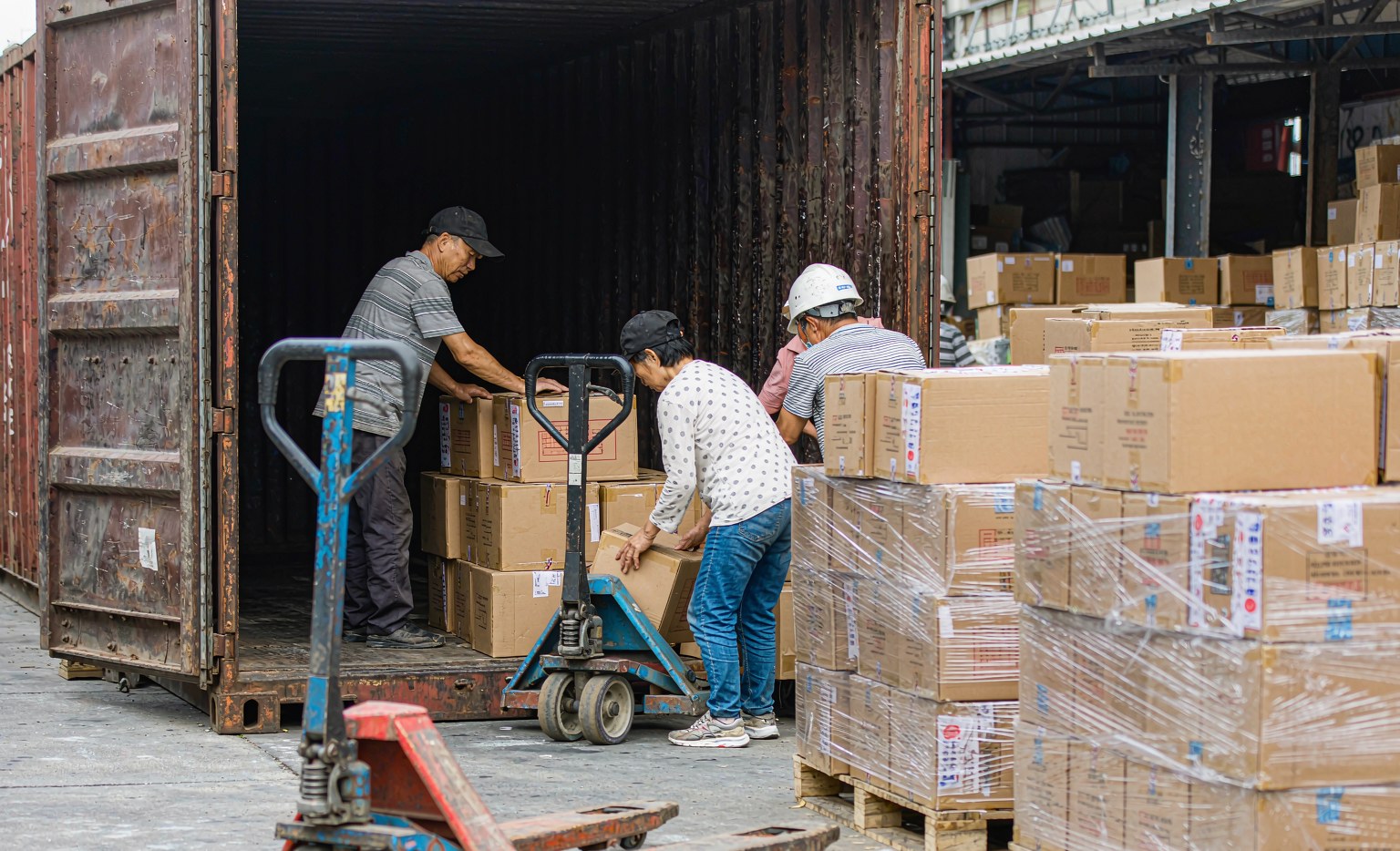 Workers loading palletised cartons of auto parts into an export container at a Guangzhou warehouse