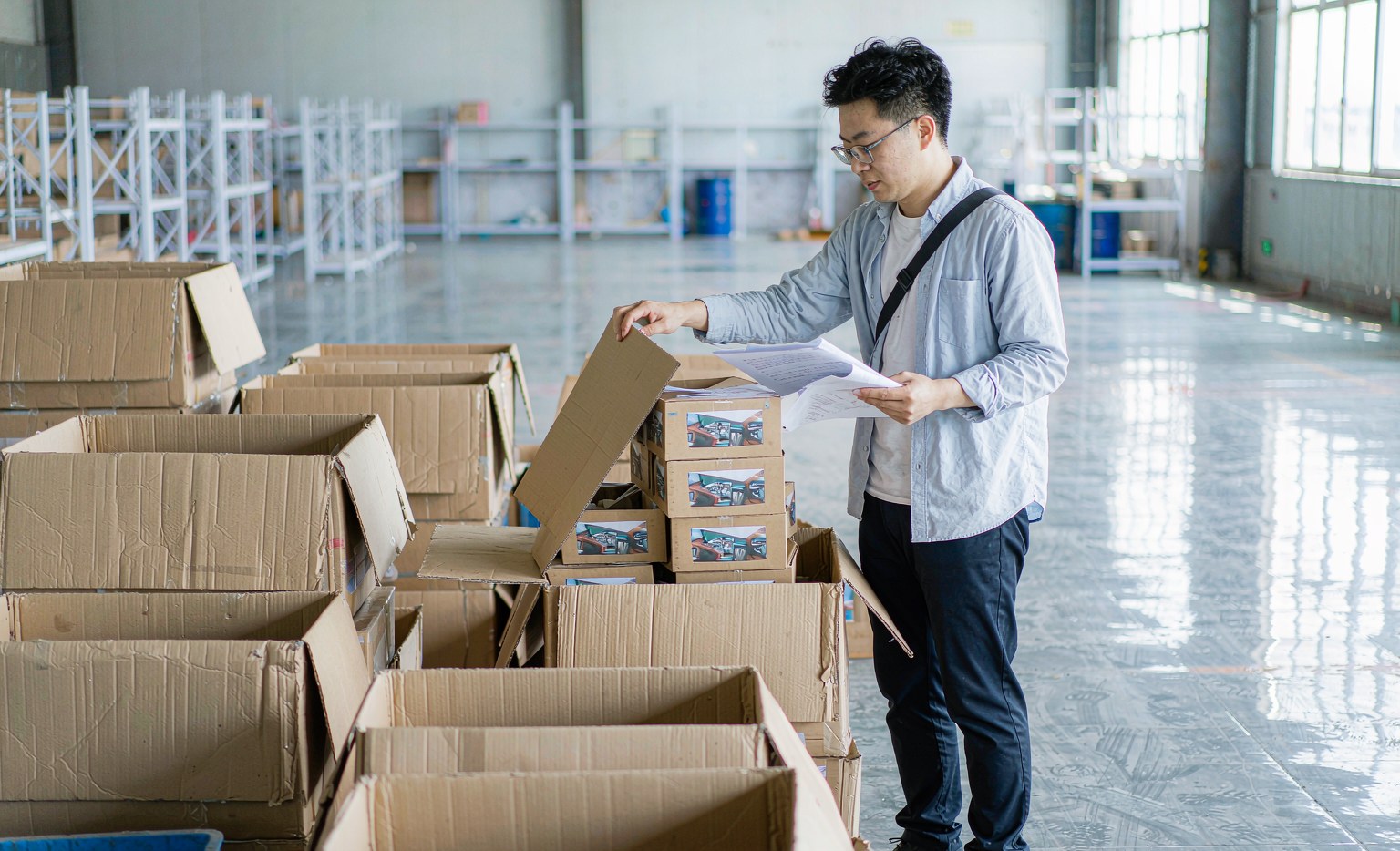 Inspector opening randomly selected cartons of packed auto parts on a factory floor with a checklist and camera