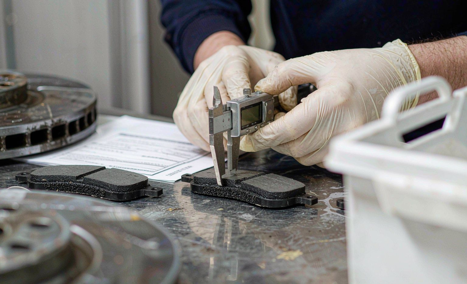 Technician measuring brake pad friction thickness with a digital caliper during incoming quality inspection