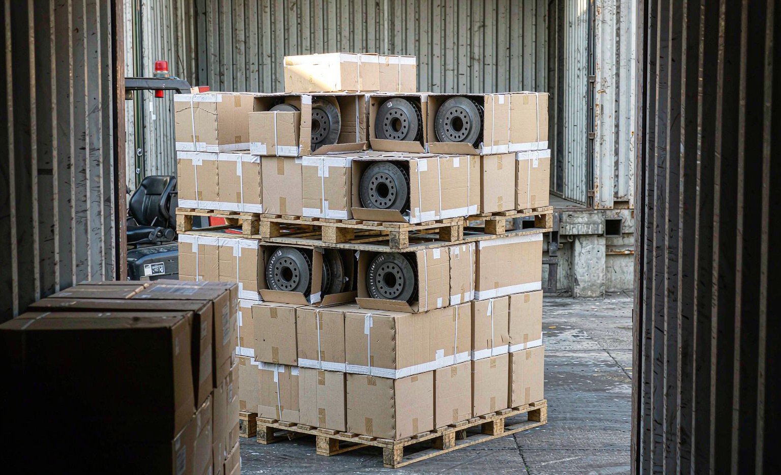 Cartons of brake pads and boxed rotors stacked on pallets being loaded into an export container