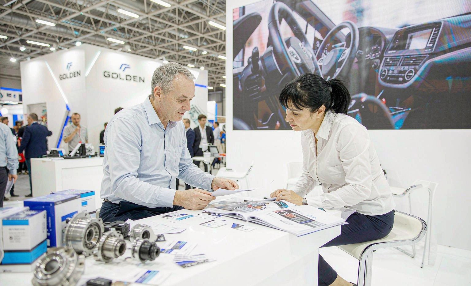 Overseas buyer reviewing an auto parts catalog with a supplier at a Canton Fair booth in the Pazhou halls