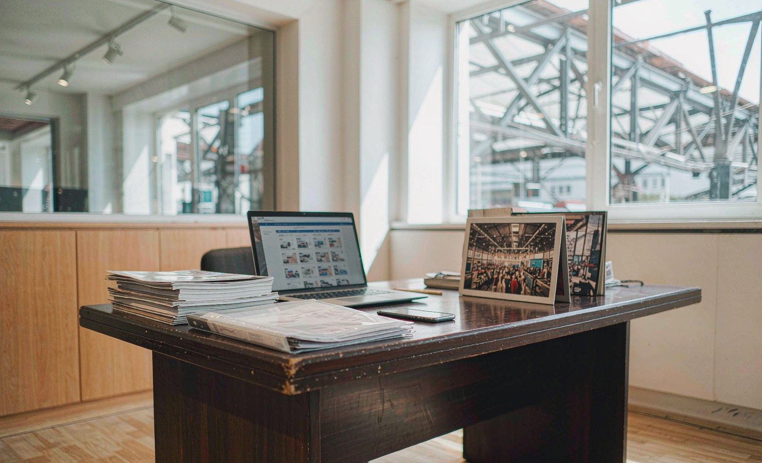 Auto parts buyer comparing online supplier listings on a laptop with paper catalogs and a trade fair photo on the desk, illustrating Canton Fair versus online sourcing for auto parts from China