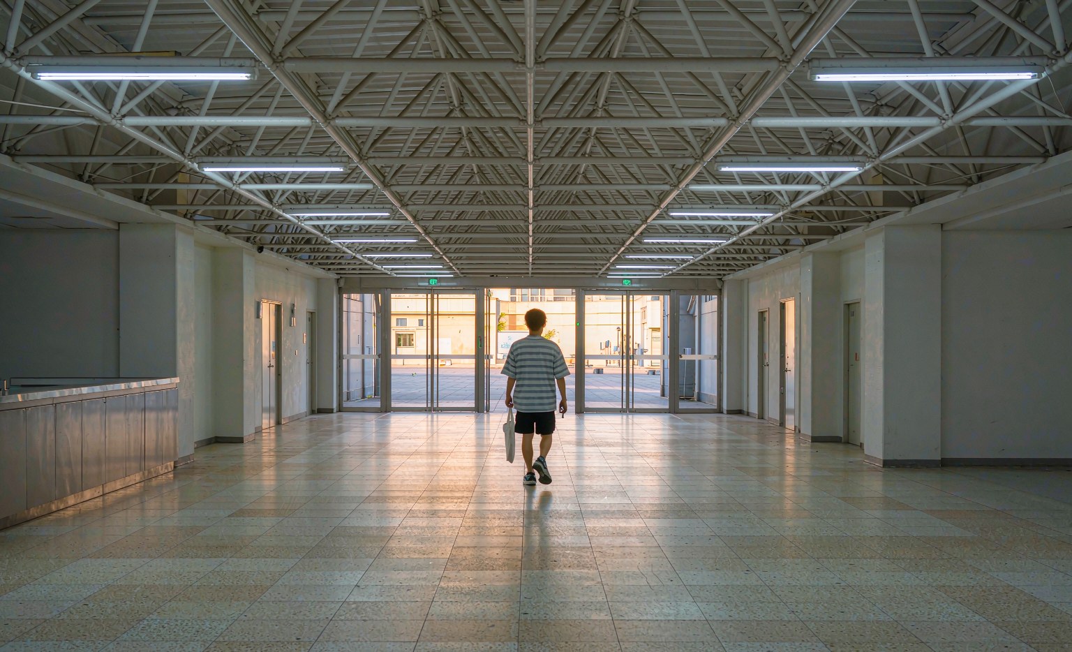 Overseas auto parts buyer walking through a quiet exhibition center corridor carrying a sample tote bag, illustrating the decision between Canton Fair and year-round online sourcing from China