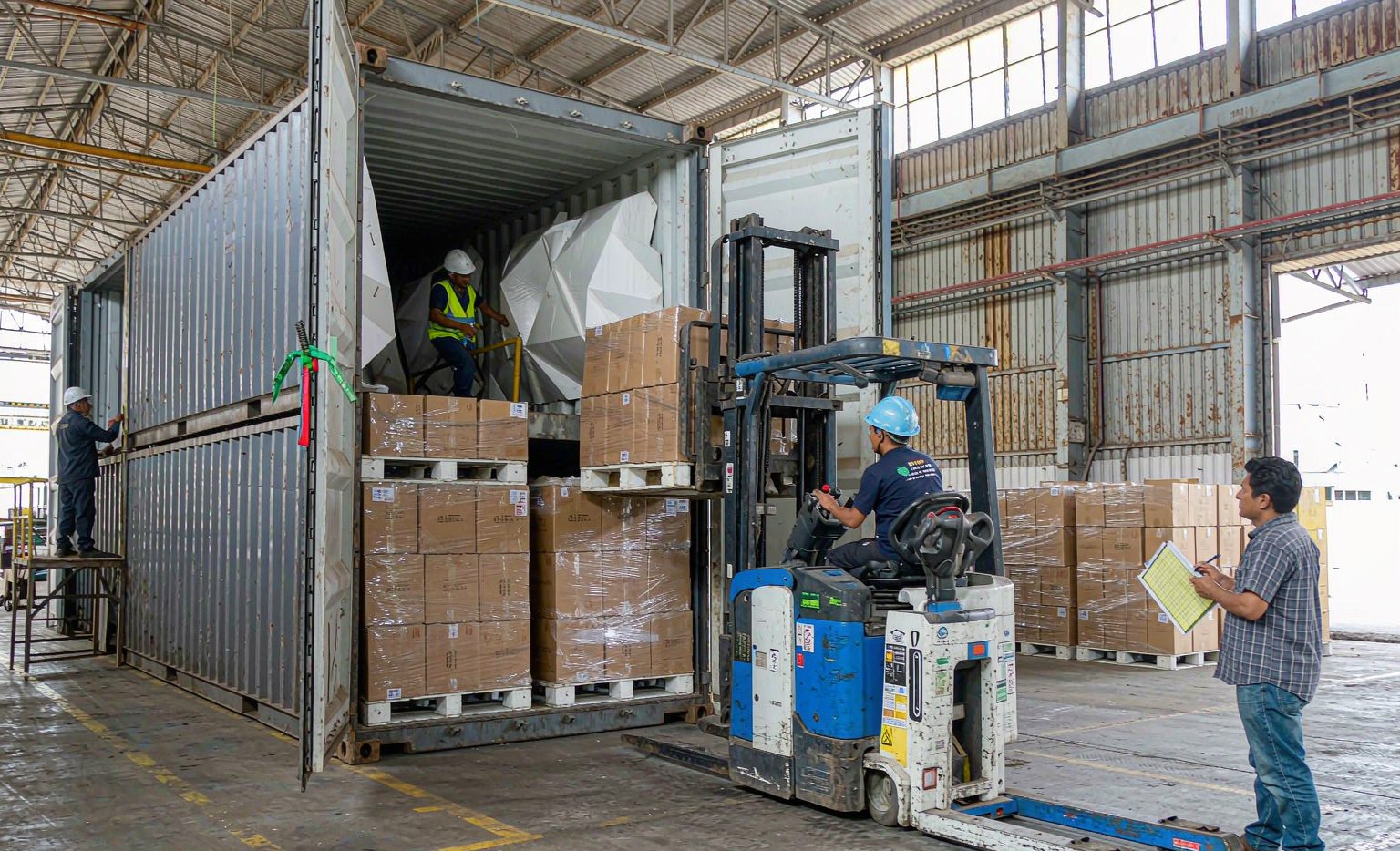 Container loading supervision with stacked auto parts cartons, a checker recording carton count and the container seal being applied