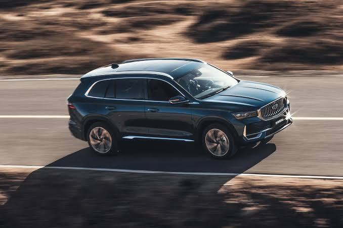 Geely Xingyue L Monjaro dark blue front side dynamic view — 2.0TD AWD SUV showing signature energy volcano grille, LED headlamps and aerodynamic profile, FOB Nansha $23,431 from Globalucar
