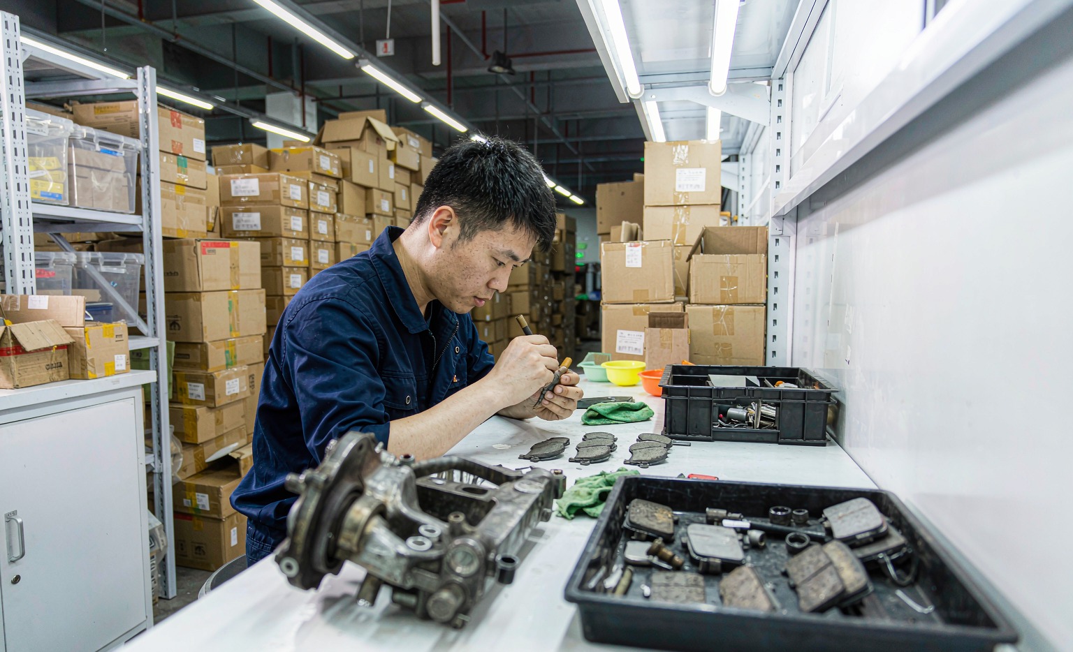 Technician inspecting brake pads and suspension parts in a clean Guangzhou auto parts warehouse