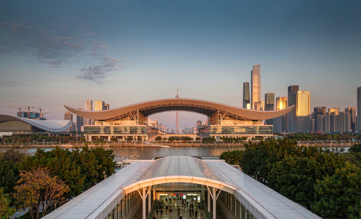 Buyers with luggage walking toward a modern metro station entrance beside the Pazhou exhibition complex in Guangzhou, illustrating a Canton Fair travel guide