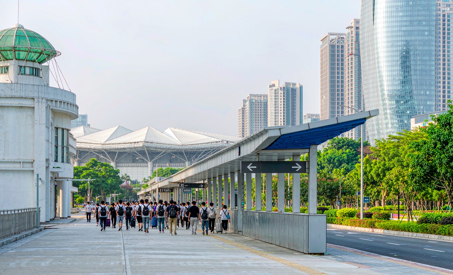 Buyers walking toward a metro station entrance beside the Pazhou exhibition complex in Guangzhou with line signage, representing getting to the Canton Fair by metro