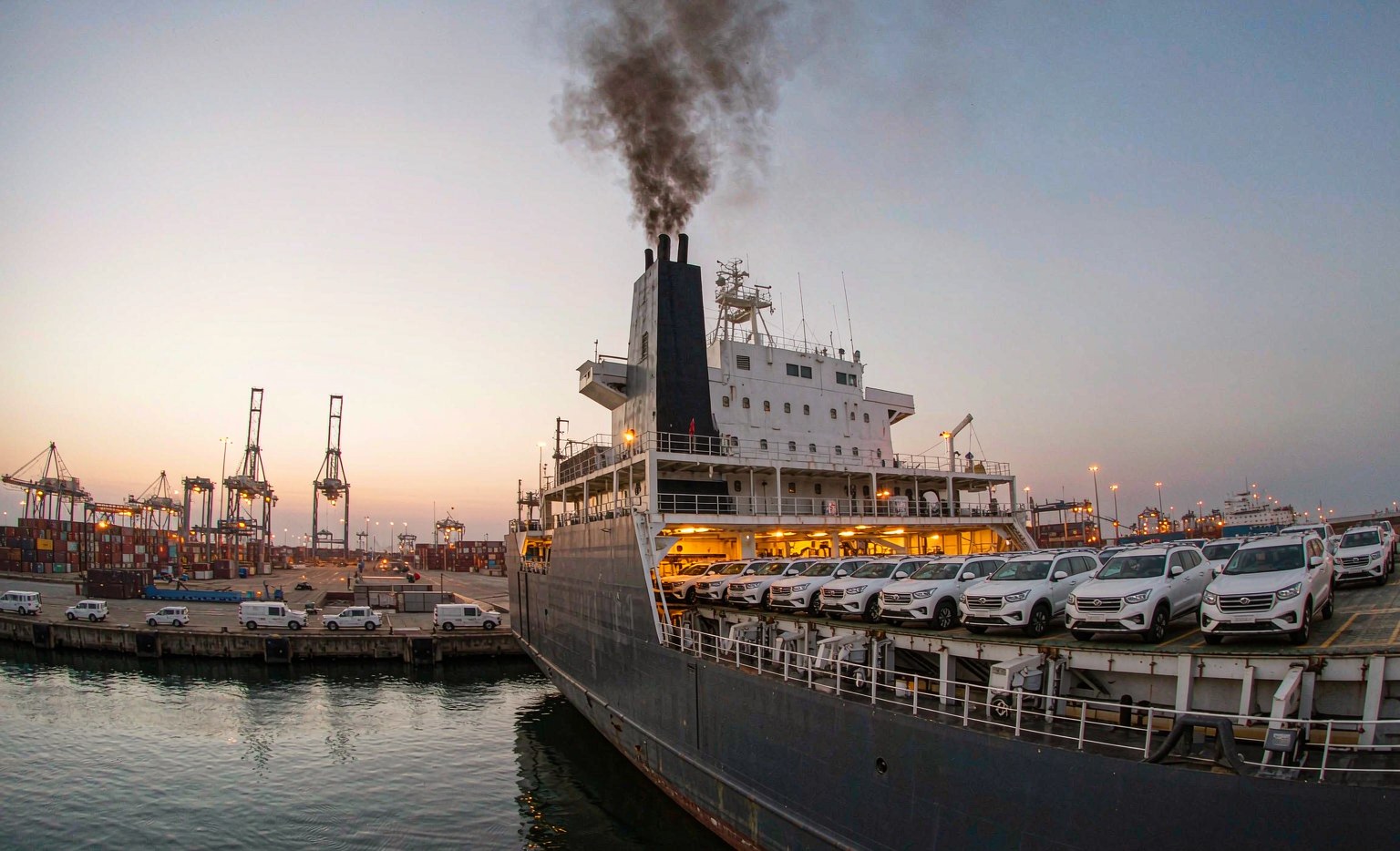 New vehicles lined up on the quay beside a roll-on roll-off car carrier at a vehicle export terminal