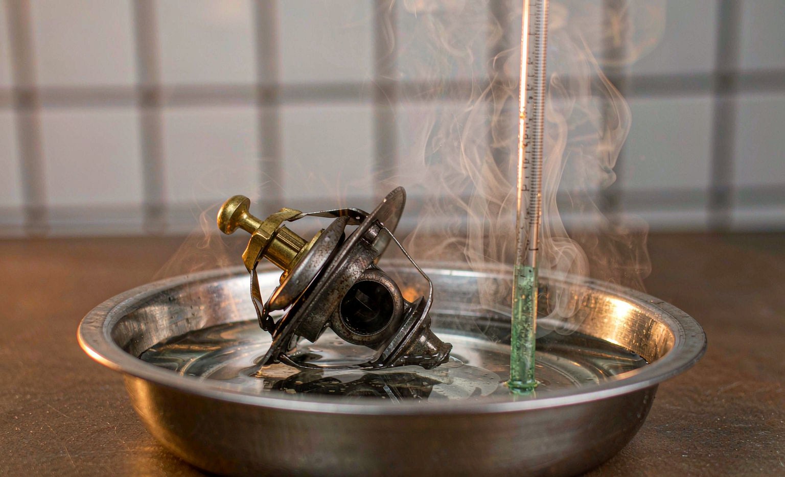 Thermostat and housing submerged in a pan of heated water with a thermometer, valve partially open