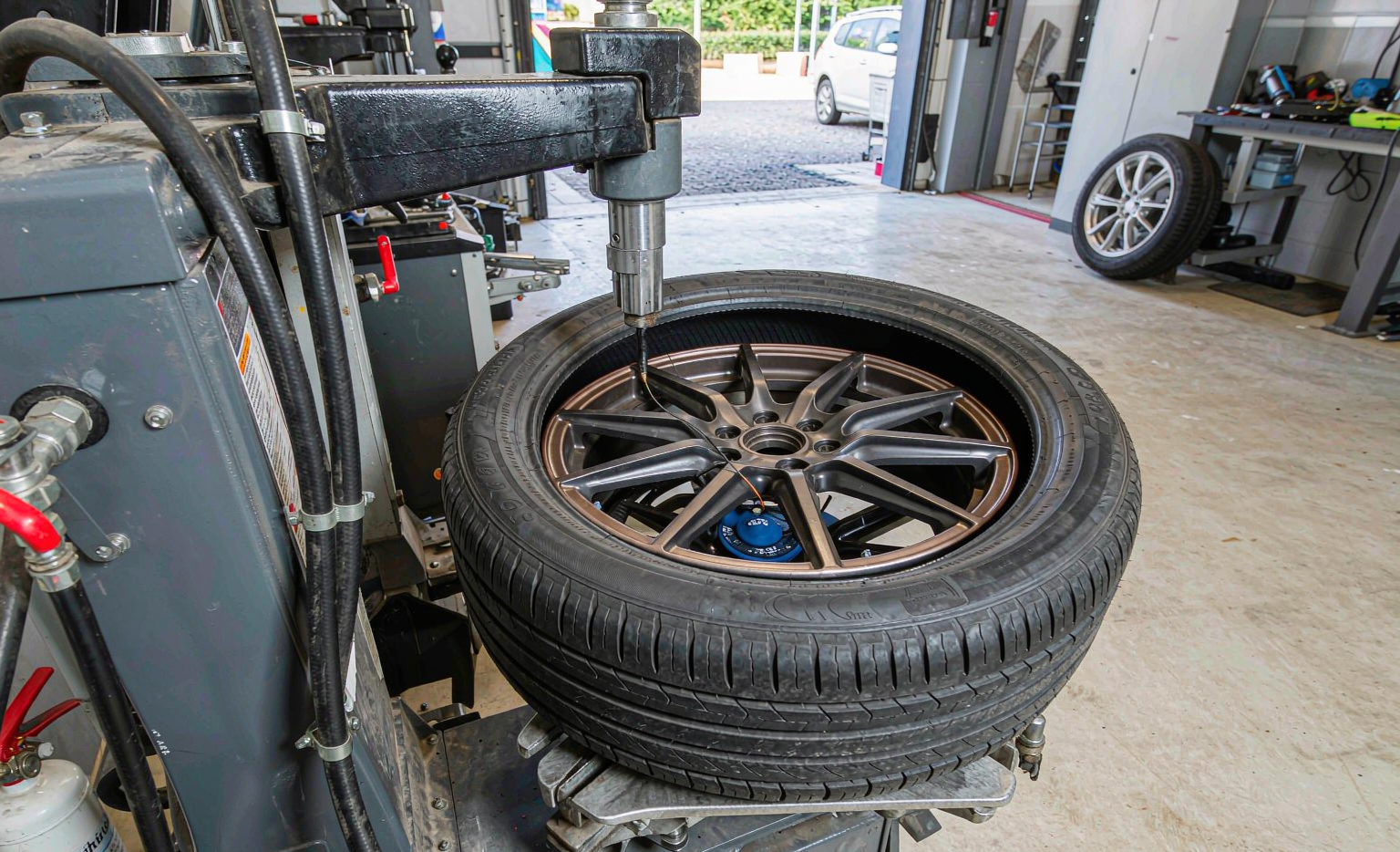 Tire being dismounted from wheel rim on tire changer machine showing TPMS sensor inside tire cavity in modern auto repair shop