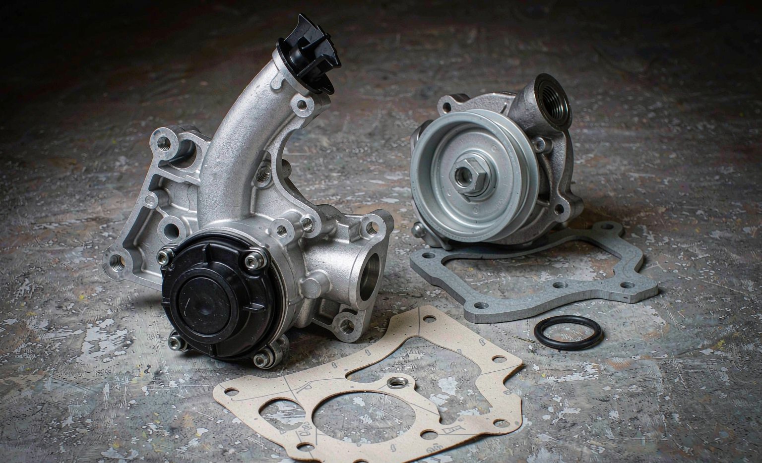 A new water pump and thermostat housing laid out on a workshop bench with their gaskets