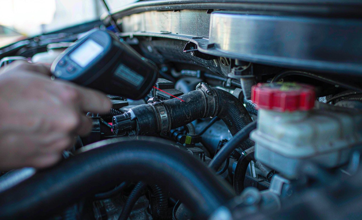 Infrared thermometer aimed at an upper radiator hose in an engine bay with the reading visible on the display